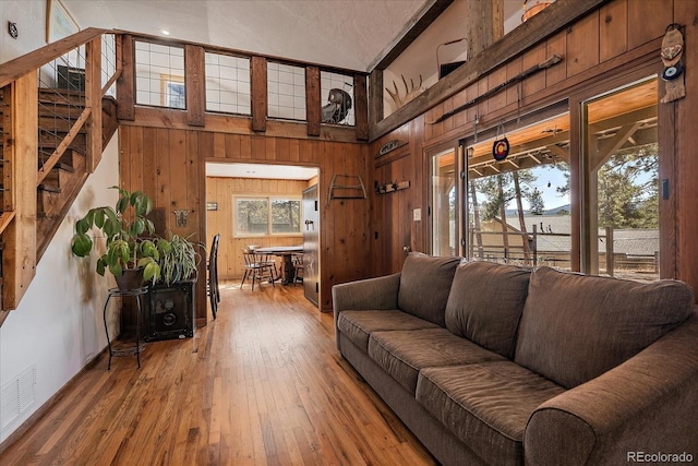 living room featuring visible vents, wooden walls, stairs, hardwood / wood-style floors, and a towering ceiling