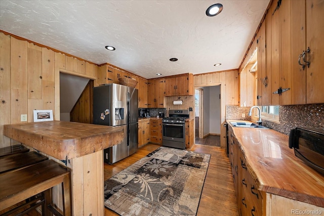 kitchen with butcher block countertops, appliances with stainless steel finishes, light wood-style floors, and a sink