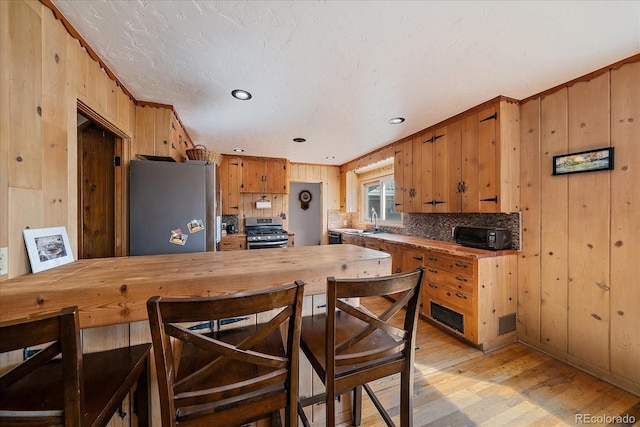 kitchen featuring appliances with stainless steel finishes, light wood-style flooring, and wood walls