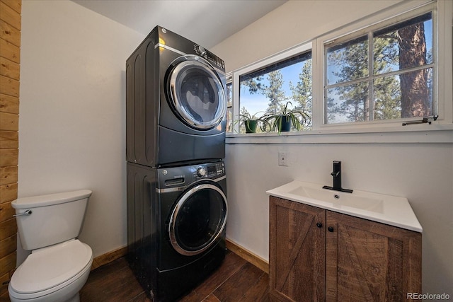 laundry area with baseboards, laundry area, dark wood-style flooring, a sink, and stacked washer and clothes dryer