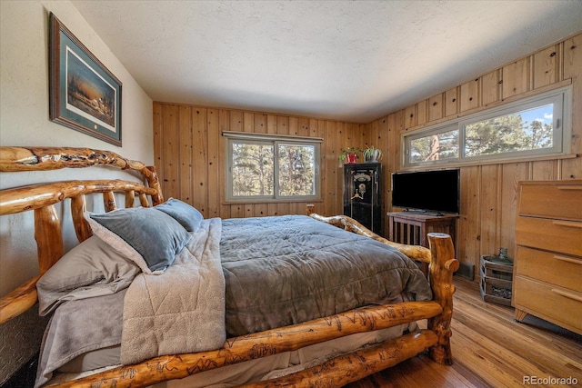 bedroom featuring wooden walls, a textured ceiling, and hardwood / wood-style floors