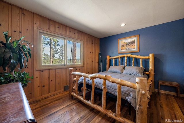 bedroom featuring visible vents, wood walls, baseboards, and wood finished floors