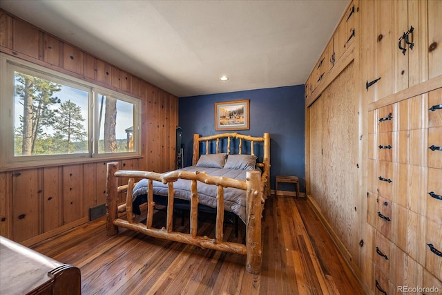 bedroom featuring visible vents, baseboards, wooden walls, and hardwood / wood-style floors