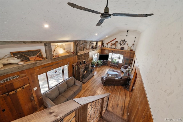 living room with lofted ceiling, a stone fireplace, wood-type flooring, a textured ceiling, and a textured wall