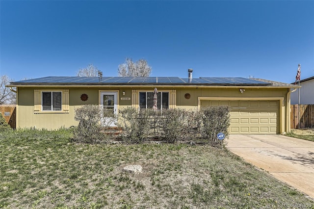 ranch-style home featuring an attached garage, roof mounted solar panels, driveway, and fence
