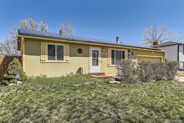 view of front of house featuring a front yard, an attached garage, fence, and solar panels