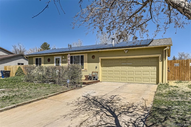 ranch-style home featuring a garage, driveway, fence, and roof mounted solar panels