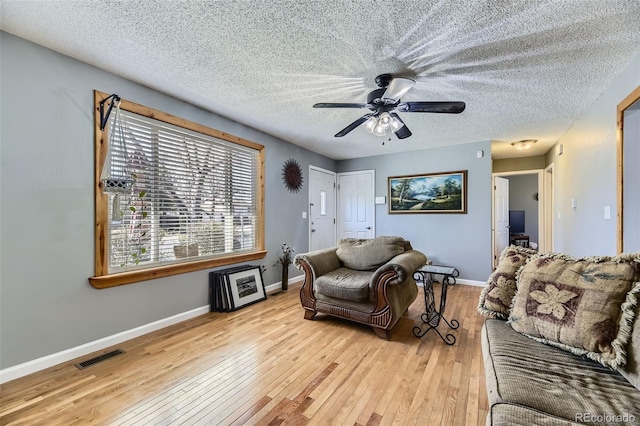 living area featuring baseboards, a textured ceiling, a ceiling fan, visible vents, and wood-type flooring