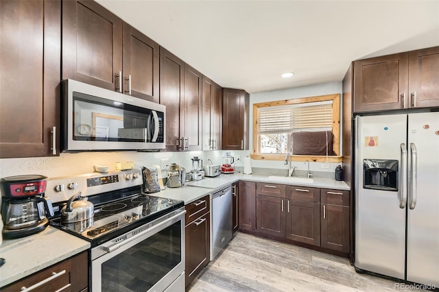 kitchen with a sink, dark brown cabinets, light wood-style flooring, and appliances with stainless steel finishes