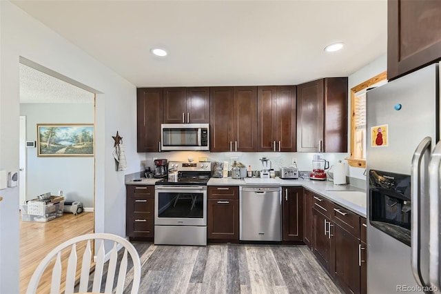 kitchen with dark brown cabinets, light countertops, light wood finished floors, and stainless steel appliances