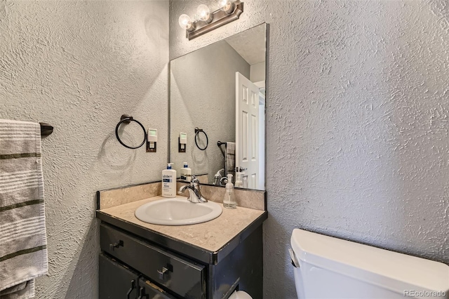 bathroom featuring a textured wall, vanity, and toilet