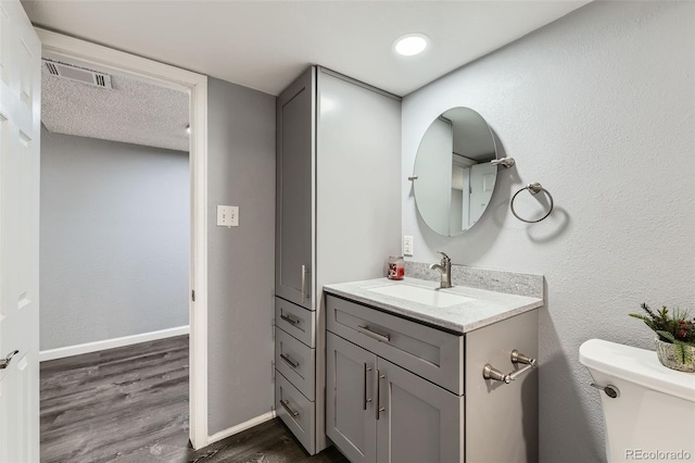 half bath with vanity, visible vents, toilet, wood finished floors, and baseboards