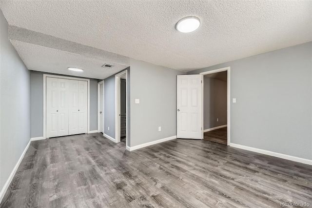 unfurnished bedroom with a textured ceiling, baseboards, and wood finished floors