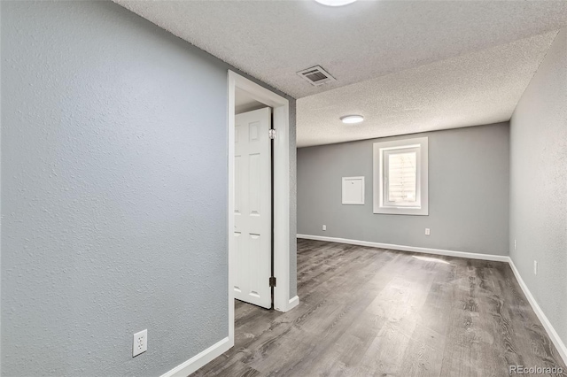 below grade area featuring visible vents, baseboards, a textured wall, a textured ceiling, and wood finished floors