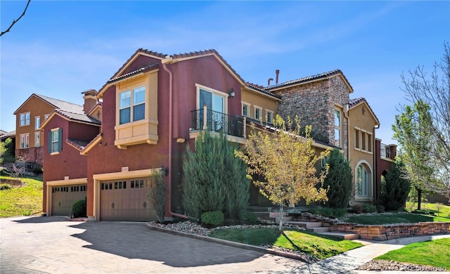 view of front of house featuring a balcony, a tiled roof, decorative driveway, an attached garage, and stucco siding