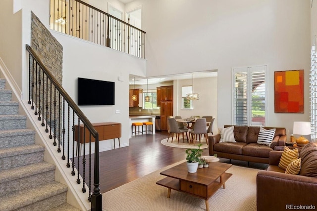living room featuring stairway, a towering ceiling, baseboards, and dark wood-style floors