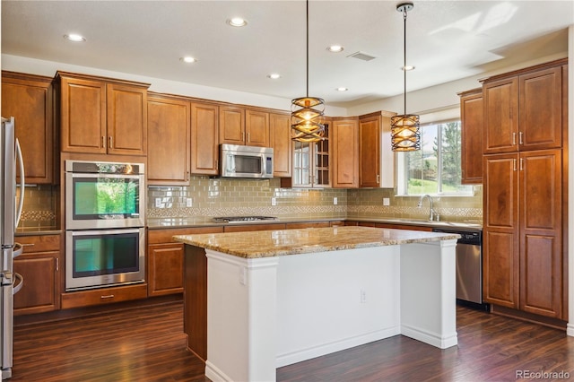 kitchen featuring brown cabinetry, stainless steel appliances, dark wood finished floors, and light stone countertops