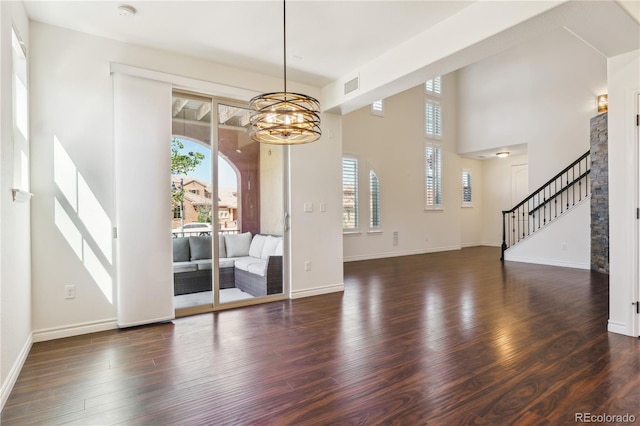 unfurnished dining area featuring visible vents, stairs, a chandelier, a towering ceiling, and dark wood-type flooring