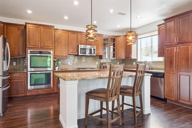 9588 Firenze Way, Highlands Ranch, CO 80126 - kitchen featuring stainless steel appliances, dark wood-style floors, light stone countertops, a kitchen island, and decorative backsplash