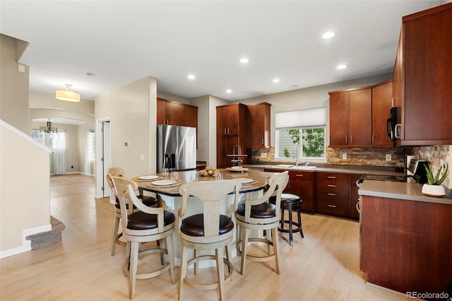 22 Apache Plume St, Brighton, CO 80601 - kitchen featuring stainless steel fridge with ice dispenser, a kitchen bar, decorative backsplash, light wood finished floors, and a kitchen island
