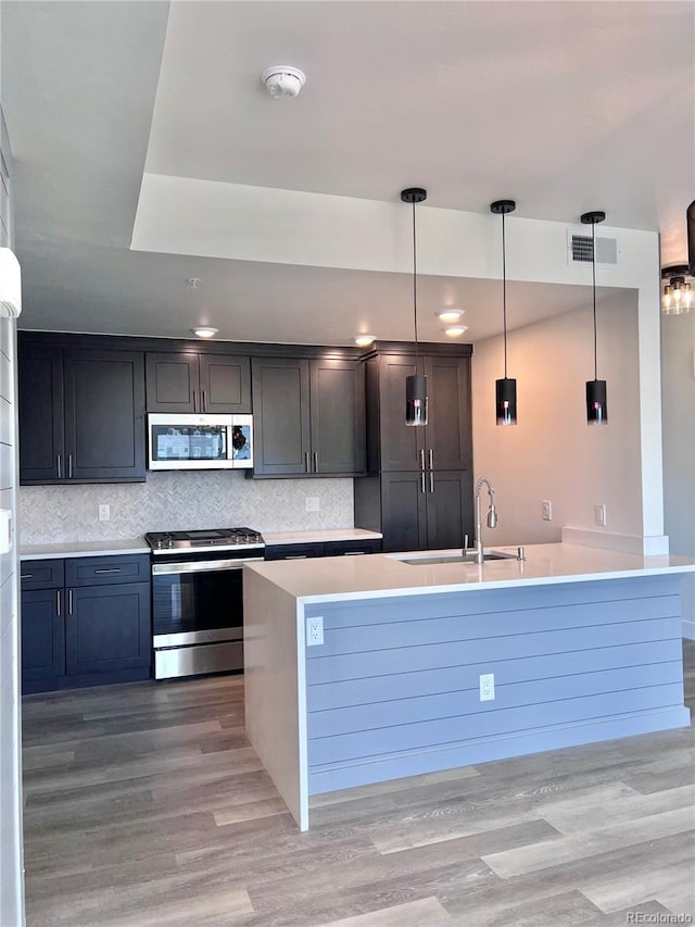 kitchen with pendant lighting, light hardwood / wood-style flooring, stainless steel appliances, sink, and decorative backsplash