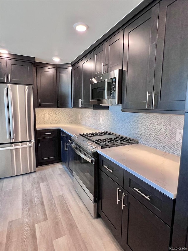 kitchen with light wood-type flooring, appliances with stainless steel finishes, and tasteful backsplash