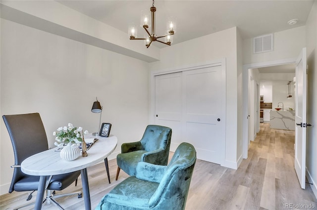 home office with light hardwood / wood-style floors and a notable chandelier