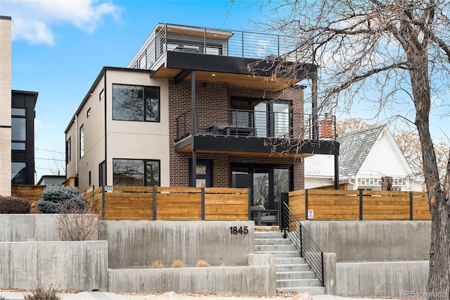 contemporary house featuring a fenced front yard, brick siding, a balcony, and stucco siding