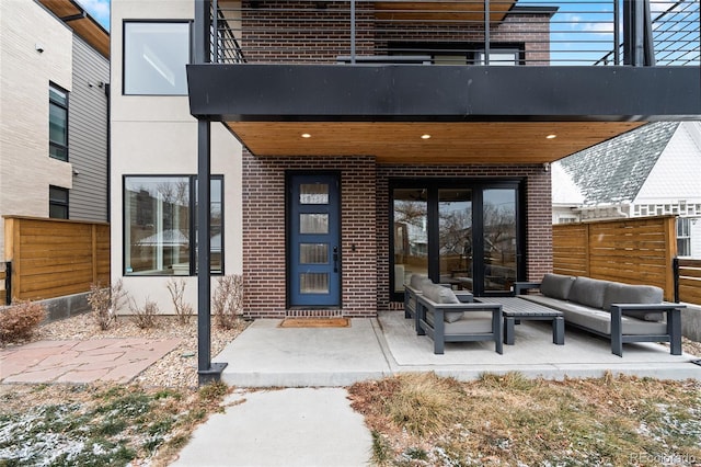 property entrance featuring outdoor lounge area, fence, a balcony, and brick siding