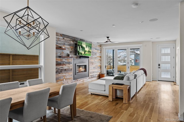 living room with light wood-type flooring, ceiling fan with notable chandelier, french doors, and a glass covered fireplace