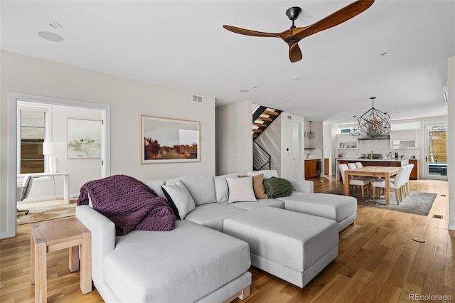 living area featuring stairway, a ceiling fan, visible vents, and light wood-style floors