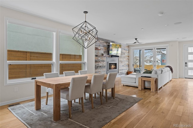 dining space with a fireplace, visible vents, baseboards, light wood-style floors, and an inviting chandelier