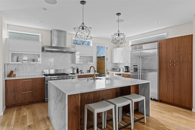 kitchen with wall chimney range hood, modern cabinets, high end appliances, and a sink