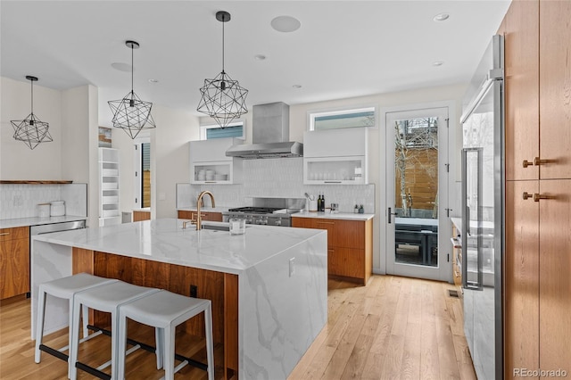 kitchen with brown cabinetry, wall chimney exhaust hood, modern cabinets, appliances with stainless steel finishes, and backsplash