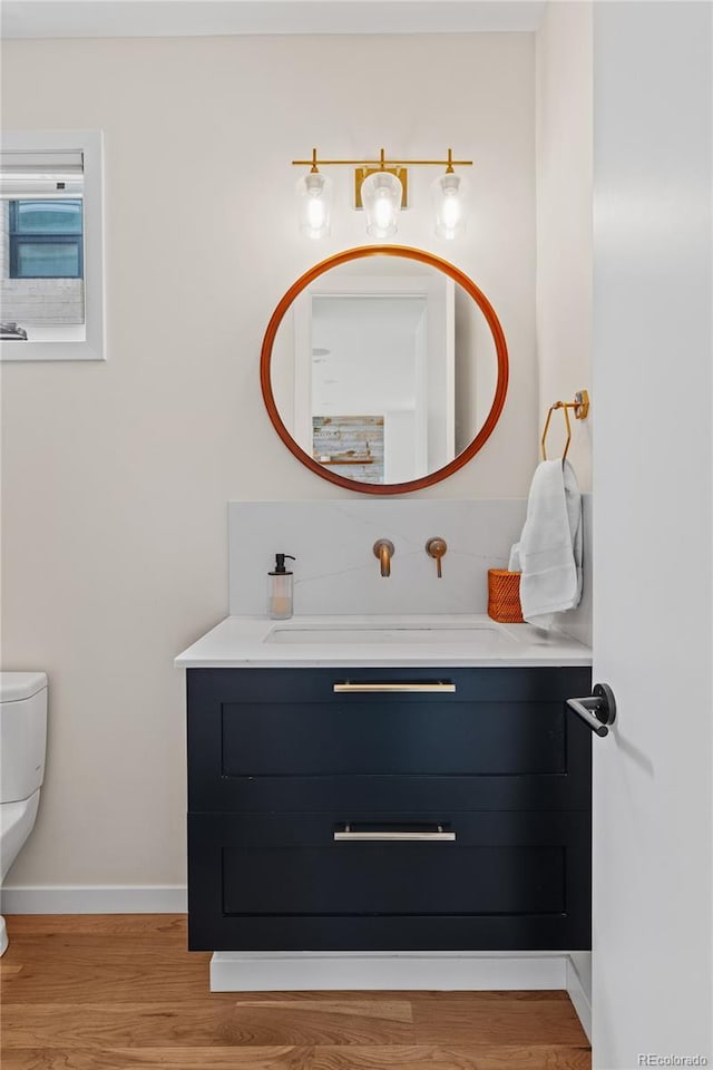 bathroom with toilet, vanity, baseboards, and wood finished floors