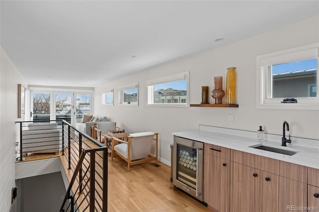 kitchen featuring beverage cooler, light countertops, a sink, and light wood-style flooring