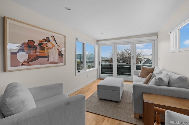 living room featuring light wood-style floors, a view of city, baseboards, and a wealth of natural light