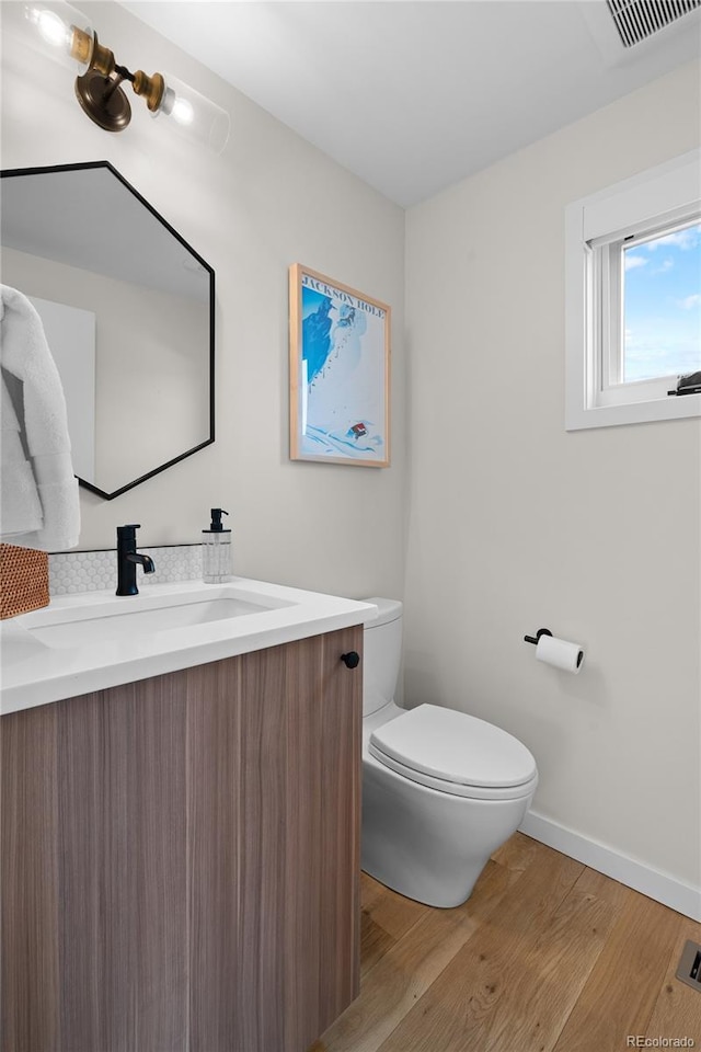 half bath featuring visible vents, toilet, vanity, wood finished floors, and baseboards