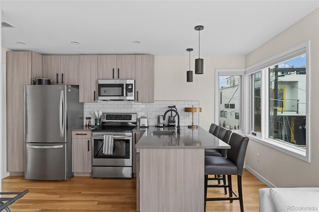 kitchen with decorative backsplash, appliances with stainless steel finishes, light wood-type flooring, a peninsula, and a kitchen bar