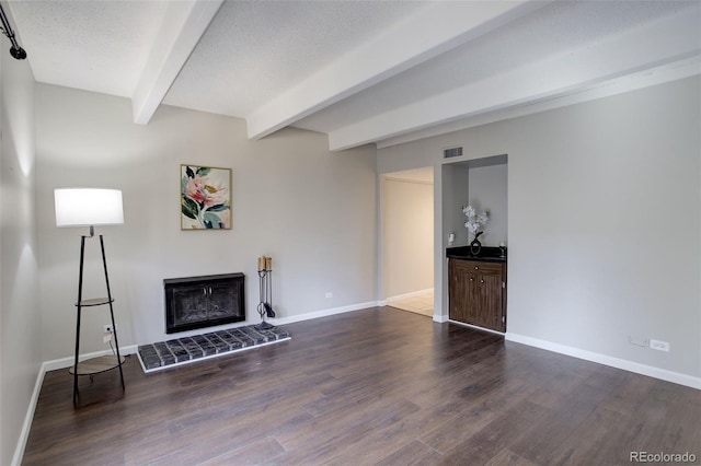 unfurnished living room featuring visible vents, a fireplace with raised hearth, beamed ceiling, wood finished floors, and a textured ceiling