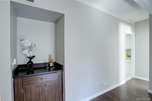 bar featuring a textured ceiling, dark wood-type flooring, and baseboards