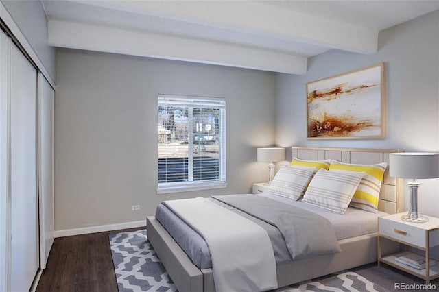 bedroom with a closet, baseboards, wood finished floors, and beamed ceiling