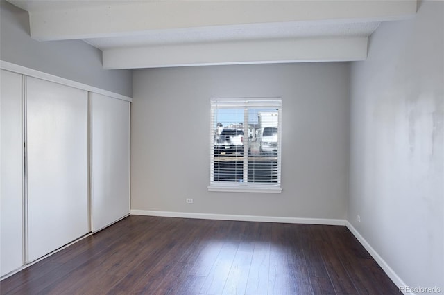 unfurnished bedroom with beamed ceiling, a closet, hardwood / wood-style flooring, and baseboards