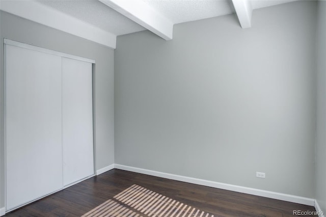 unfurnished bedroom with dark wood-style floors, a textured ceiling, baseboards, and beamed ceiling