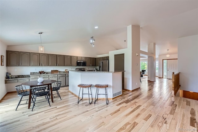 5394 S Valdai Way, Aurora, CO 80015 - kitchen featuring appliances with stainless steel finishes, light wood-style floors, a kitchen bar, a kitchen island with sink, and high vaulted ceiling