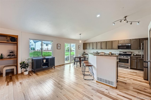 5394 S Valdai Way, Aurora, CO 80015 - kitchen with appliances with stainless steel finishes, light wood finished floors, vaulted ceiling, a breakfast bar, and a kitchen island
