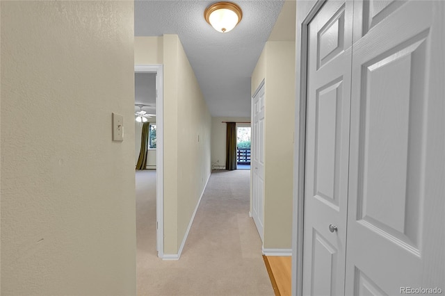 hallway featuring a textured ceiling and light colored carpet