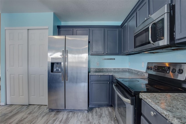 kitchen featuring light stone countertops, a textured ceiling, light wood-type flooring, and appliances with stainless steel finishes