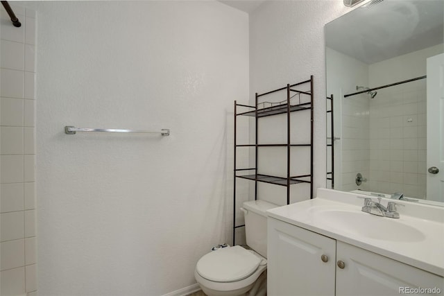 bathroom featuring toilet, tiled shower, and vanity