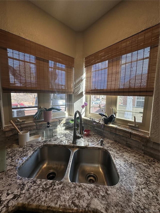 kitchen with a sink, stone counters, plenty of natural light, and a textured wall